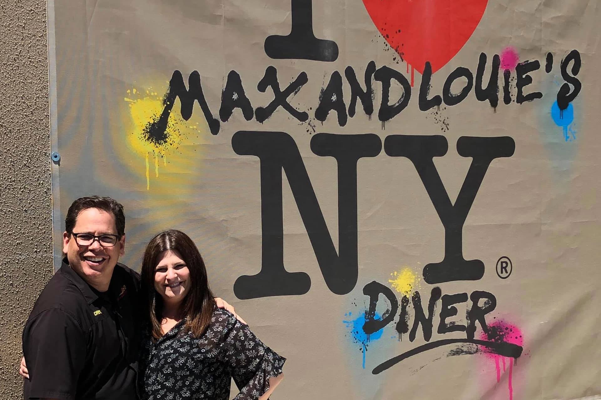 Owners of Max and Louie's New York Diner standing in front of graffiti signage